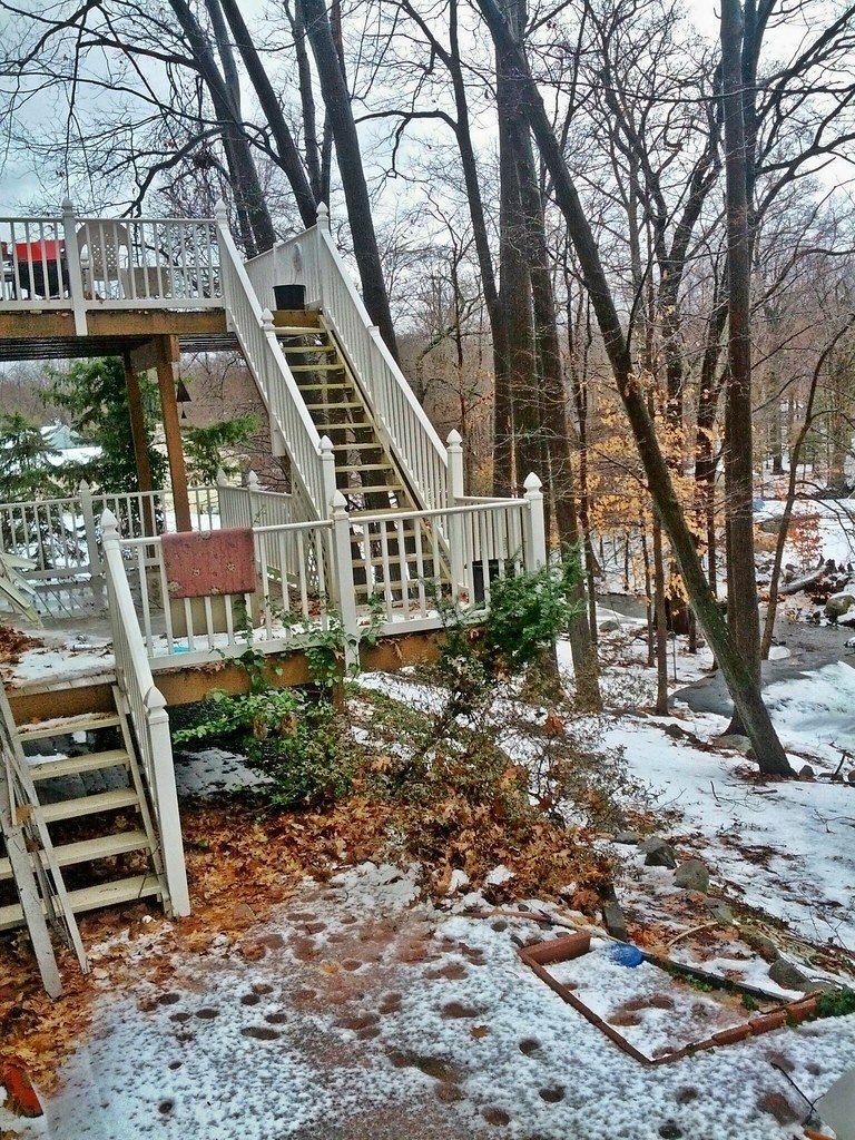 Elevated white deck with stairs in a wooded backyard